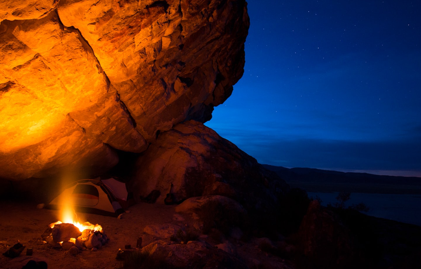 Un feu de camp illuminé se trouve à côté d'une tente sous un surplomb rocheux.