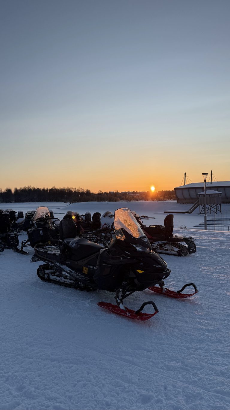 Motoneiges alignées sur un lac gelé au coucher du soleil à Rovaniemi