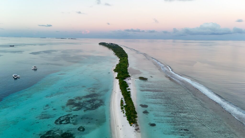 Vue au drone de l'île de Dhigurah aux Maldives, sa longue plage de sable blanc et son lagon turquoise au coucher du soleil