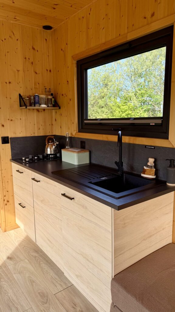 Cuisine en bois clair de la tiny house équipée d'un évier noir et d'une bouilloire