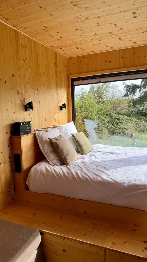 Chambre cosy de la tiny house avec lit double face à une baie vitrée sur la nature
