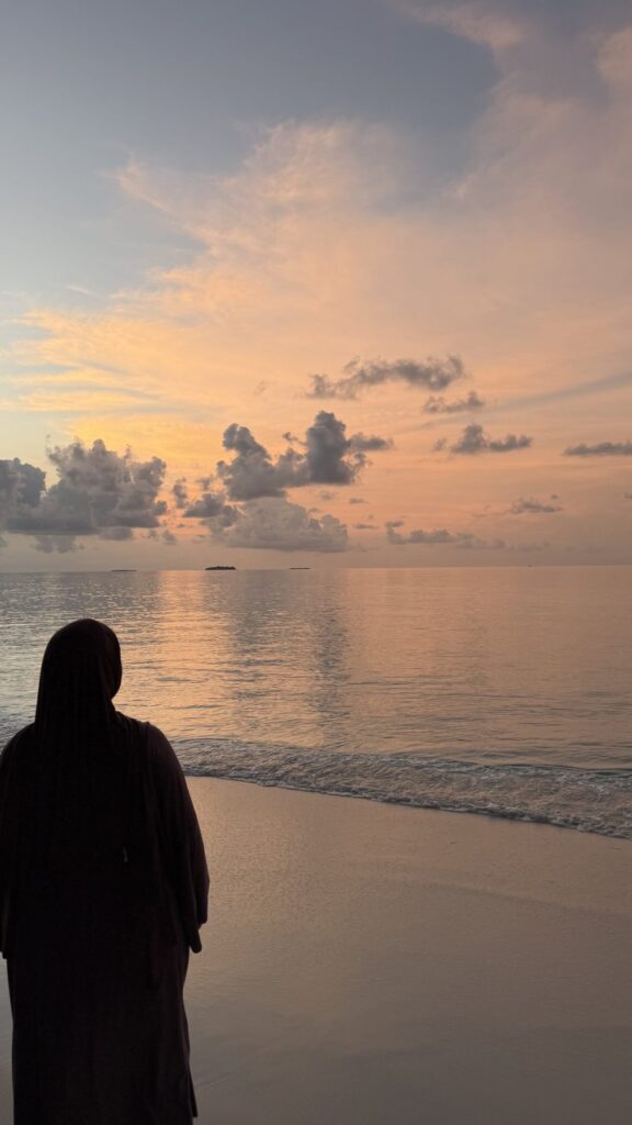 Femme en tenue couvrante face au coucher de soleil sur la plage à Maalhos aux Maldives
