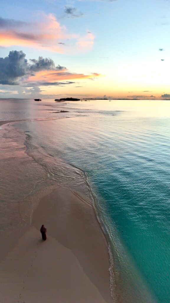 Silhouette sur la plage de sable blanc de Dhigurah aux Maldives, face au lagon turquoise au coucher du soleil