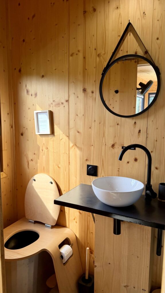 Salle de bain de la tiny house avec vasque, miroir rond et toilettes sèches