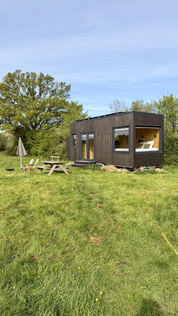 Tiny house en bois avec terrasse, parasol et coin pique-nique dans la prairie